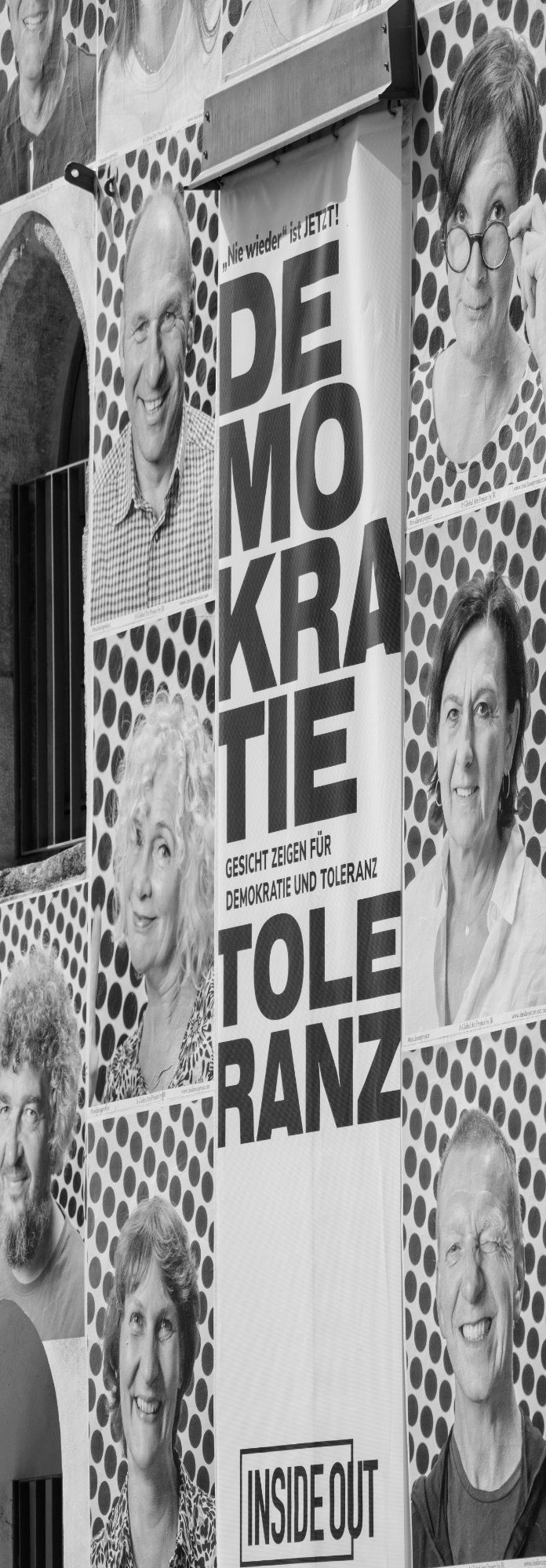 Wandinstallation mit Porträtfotos und zentralem Plakat mit den Worten ‚DEMOKRATIE‘ und ‚TOLERANZ‘.