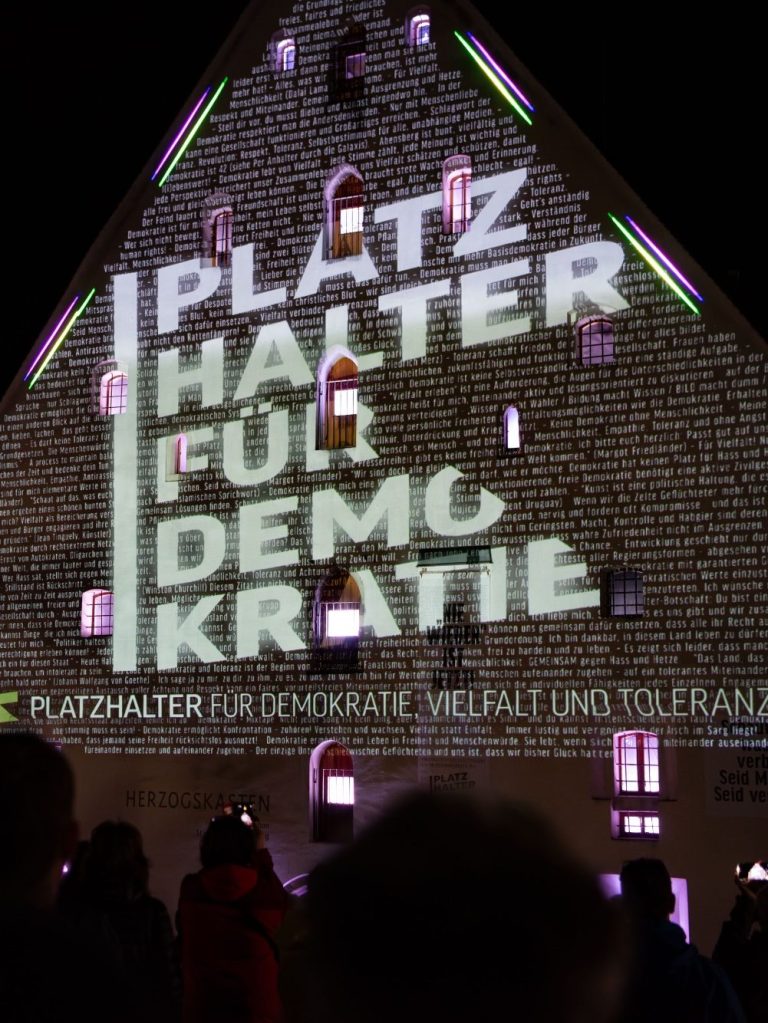 Fassade des Herzogskastens mit Projektion ‚PLATZHALTER DEMOKRATIE‘ und ‚PLATZHALTER FÜR DEMOKRATIE, VIELFALT UND TOLERANZ‘.