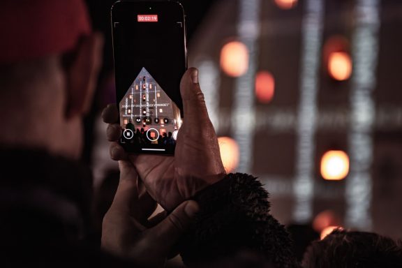 Person filmt mit Smartphone die Licht- und Laserinstallation an der Fassade des Herzogskastens.