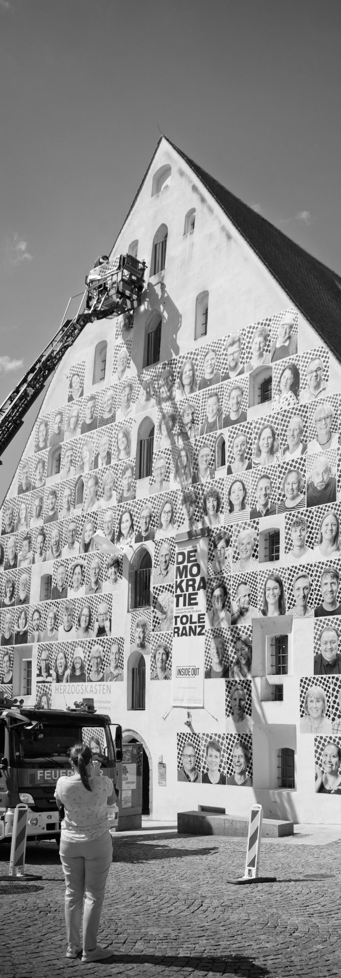 Fassade des Herzogskastens mit InsideOut-Porträts, Personen auf Drehleiter und zuschauende Menschen.