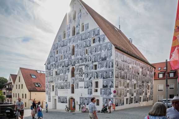 Herzogskasten mit Giebeldach, Fassade bedeckt mit zahlreichen schwarz-weißen Porträtfotos.