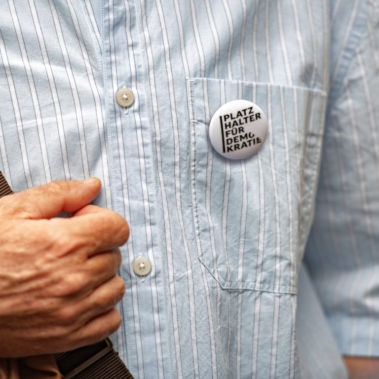 Haltung zeigen für Demokratie, Vielfalt und Toleranz Nahaufnahme eines Hemds mit einer Brusttasche, an der ein runder Button mit der Aufschrift 'PLATZ HALTER FÜR DEMOKRATIE' befestigt ist