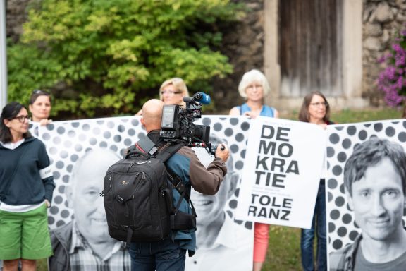 BR Kameramann filmt Gruppe, die Banner mit ‚DEMOKRATIE TOLERANZ‘ vor alter Steinmauer hält.