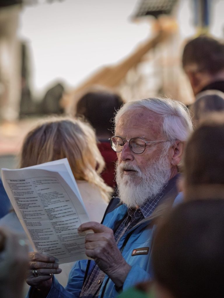 Mehrere Personen im Freien, eine hält ein Blatt mit Liedtexten und singt im PopUp-Chor.