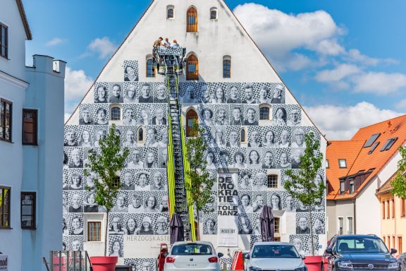 Fassade des Herzogskastens mit großflächiger Schwarz-weiß-Fotocollage, davor Drehleiter mit Personen im Korb.