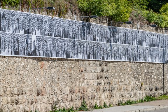 Zahlreiche schwarz-weiße Porträtfotos sind an einer alten Stadtmauer angebracht.