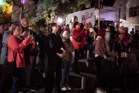 Gruppe von Menschen steht und sitzt auf Stufen und blickt auf Licht- und Laserinstallation am Herzogskasten.