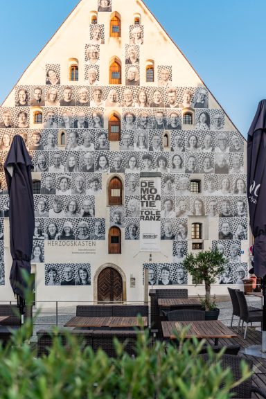 Fassade des Herzogskastens mit zahlreichen schwarz-weißen Porträtfotos von Bürger*innen als Ausstellung.